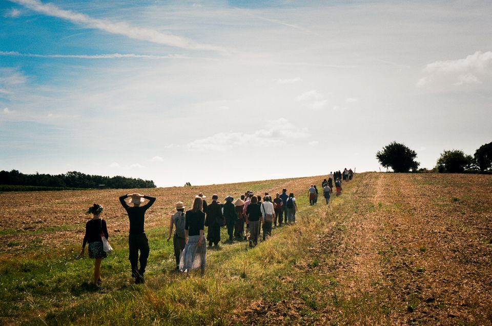 photo of about 50 people walking along a path through a field on a sunny day