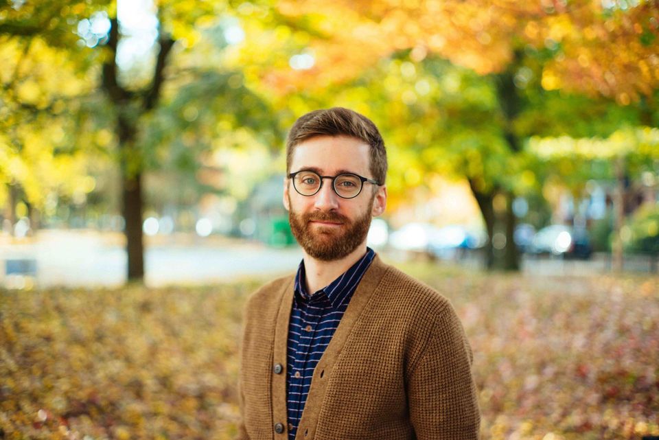 headshot photo of Robert Walsh, wearing glasses, a blue striped collar shirt, and a brown sweater