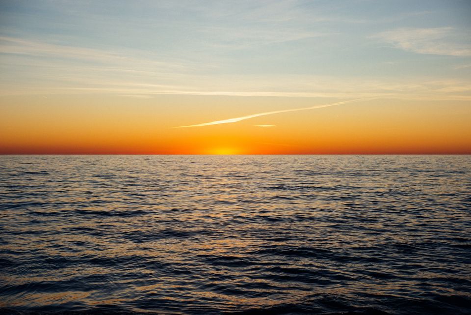 Image of a sunset over water with sparse clouds above